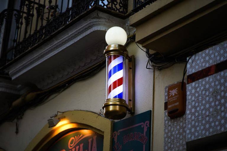 Poste de barbearia listrado em vermelho, azul e branco na fachada