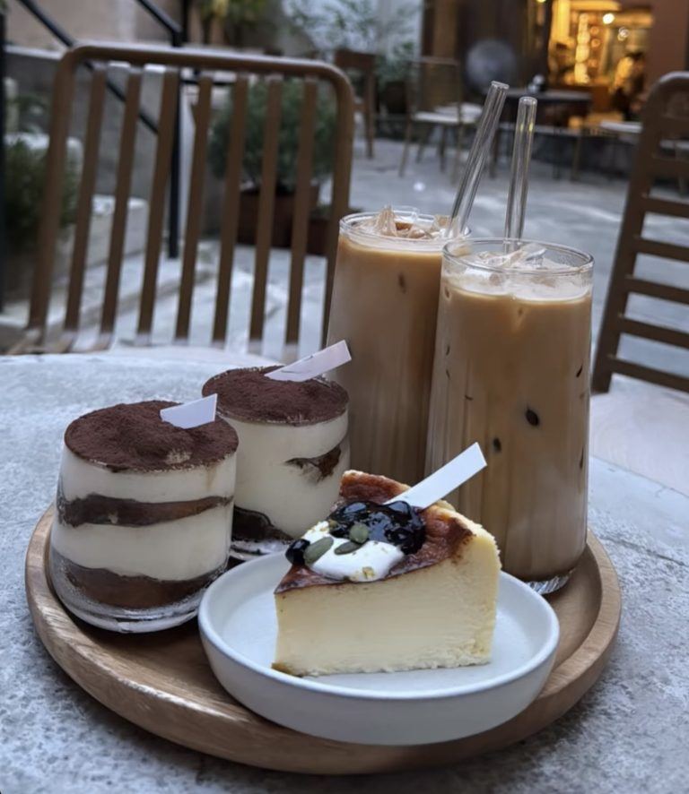 Tiramisù em copinhos e fatia de cheesecake de mirtilo, com cafés gelados ao fundo