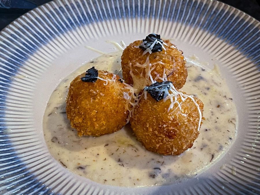 Três arancini dourados sobre creme de queijo com trufa